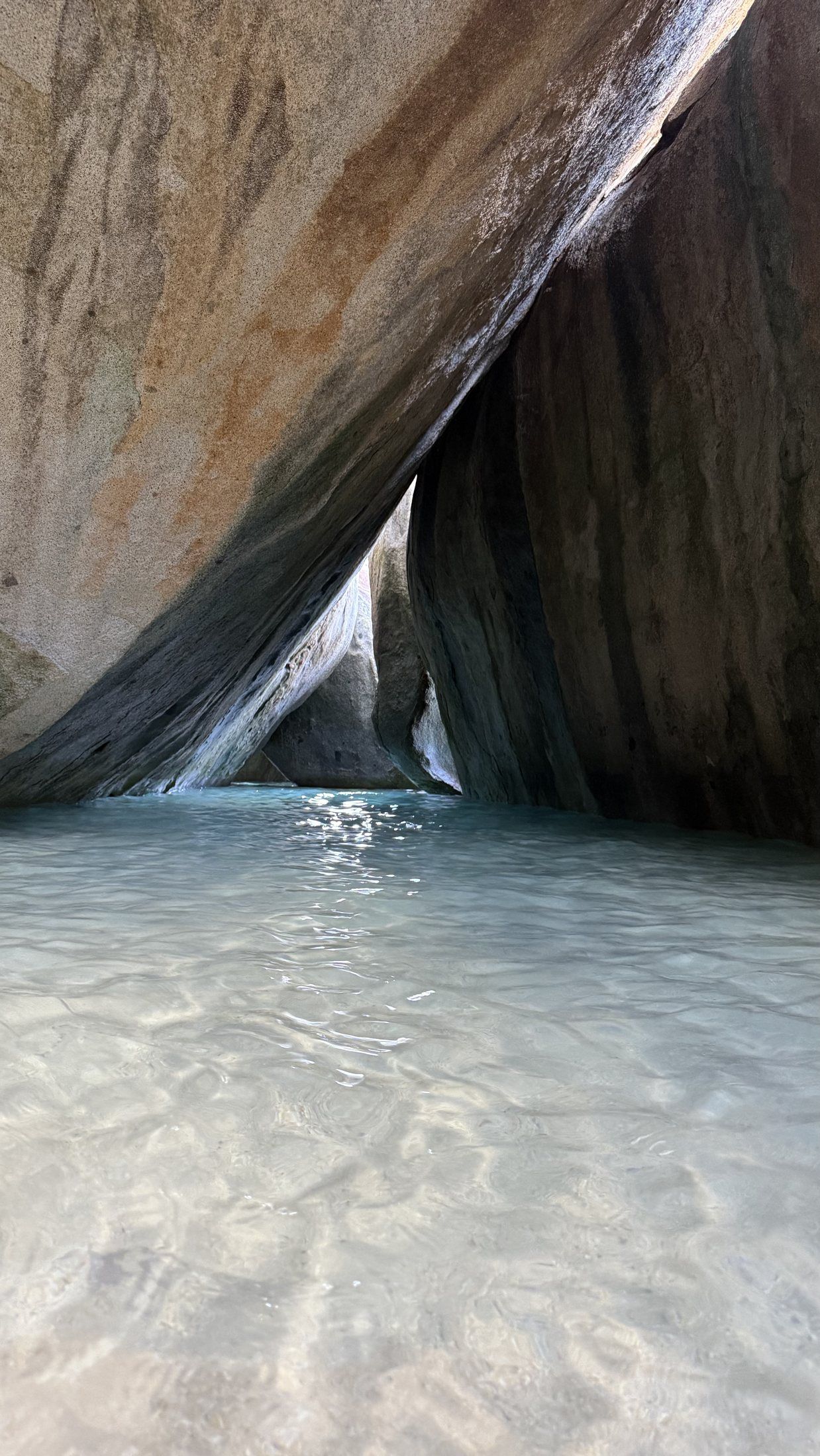 A sunlit passage between towering granite boulders at The Baths, Virgin Gorda, opening onto calm turquoise shallows.